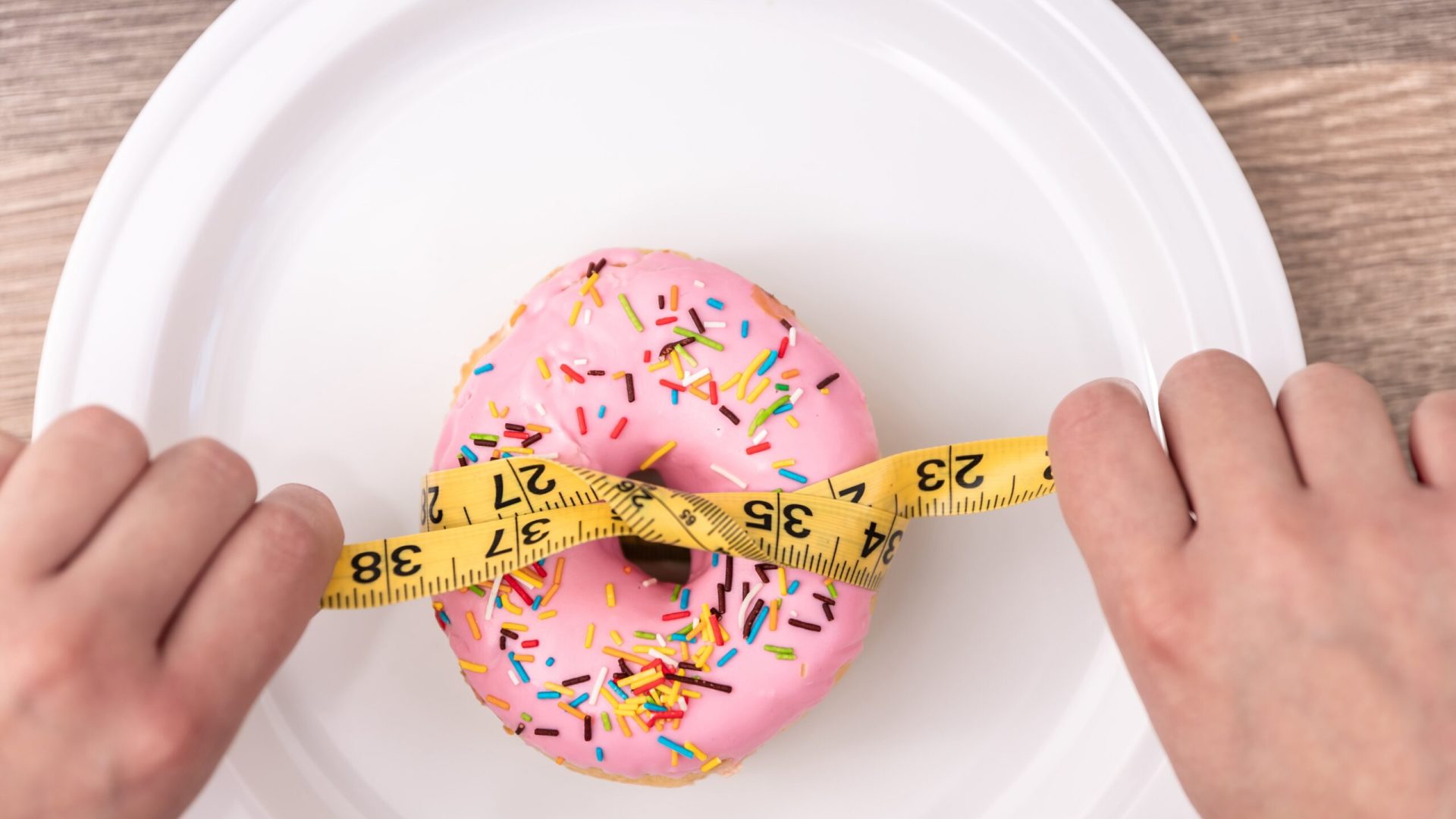 Close up of donut and measuring tape on white background, concept of weight loss, diet, obesity and weight gain.