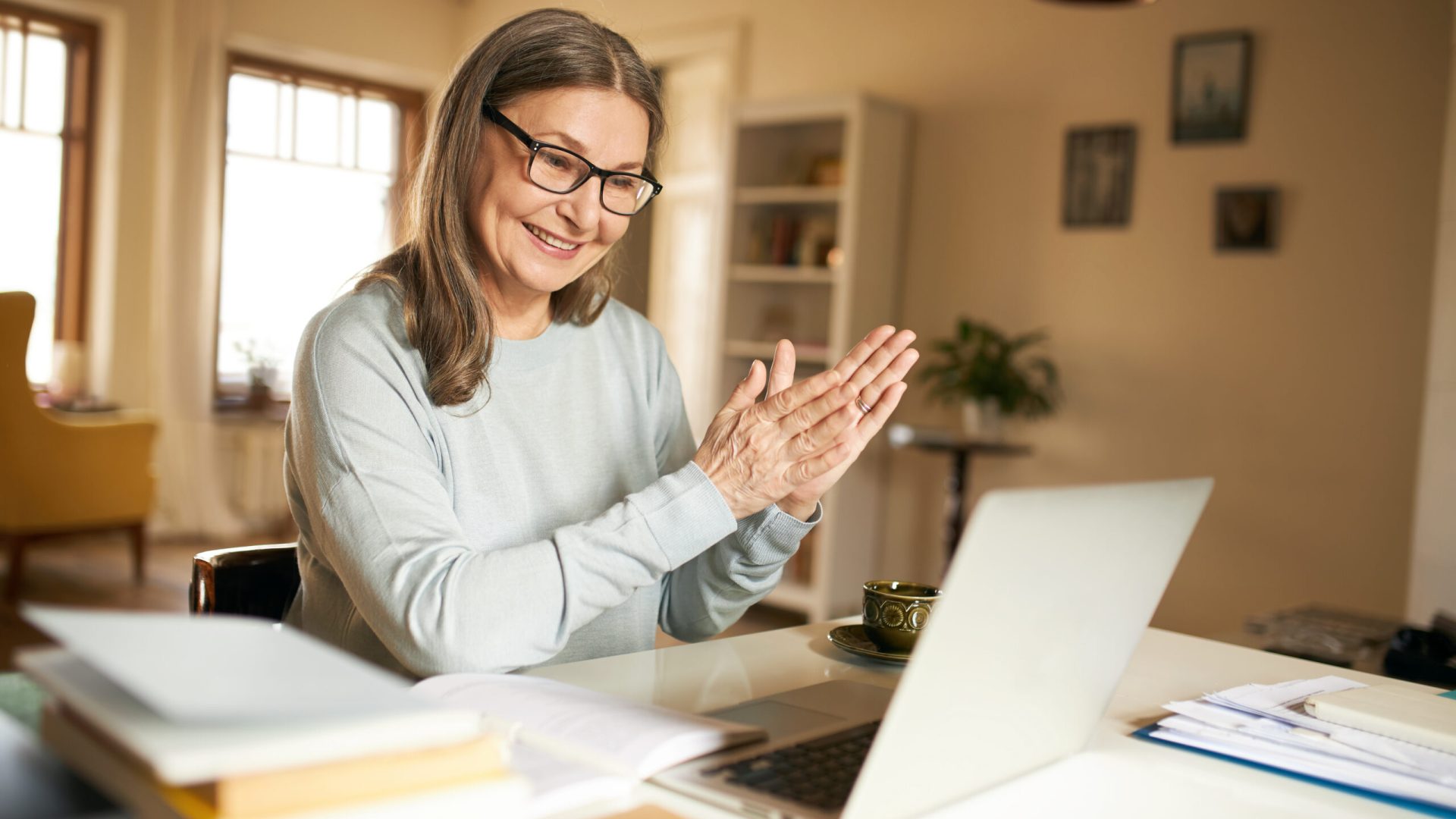 Technology, online communication and electronic gadgets concept. Positive joyful female pensioner in spectacles using laptop talking to family via webcam video conference chat, smiling, clapping hands